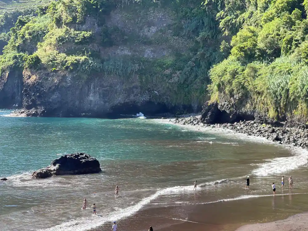 Black sand beach cove with turquoise water and steep cliffs