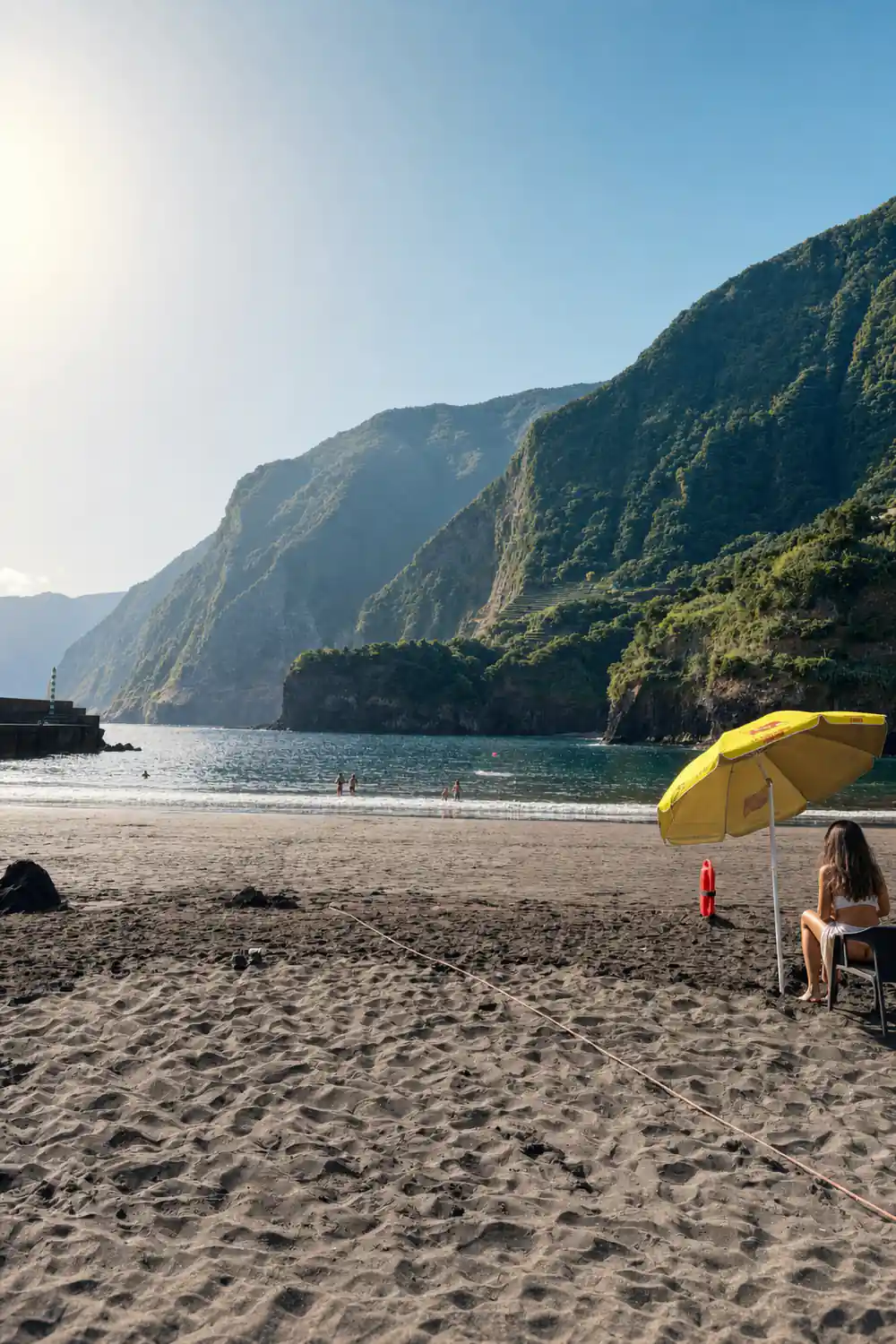 Black sand beach with yellow umbrella beneath tall sea cliffs