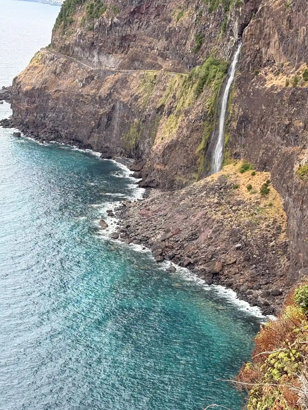 Coastal cliff with waterfall cascading into turquoise sea