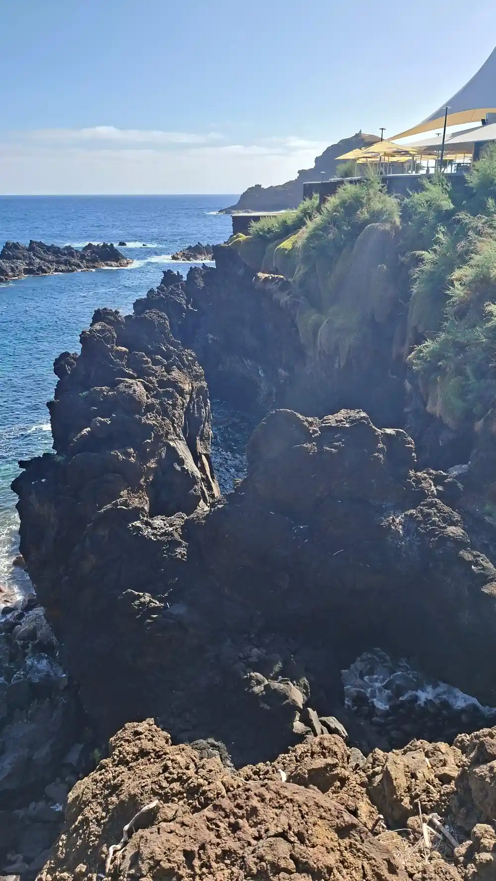 Dark stone arch bridge spanning blue ocean water