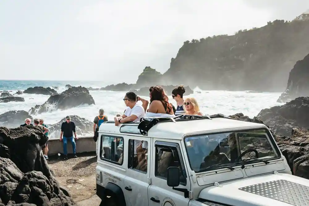 Group sitting on vehicle roof at rocky coastal viewpoint