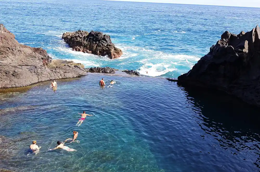 Multiple swimmers in natural rock pool surrounded by dark rocks