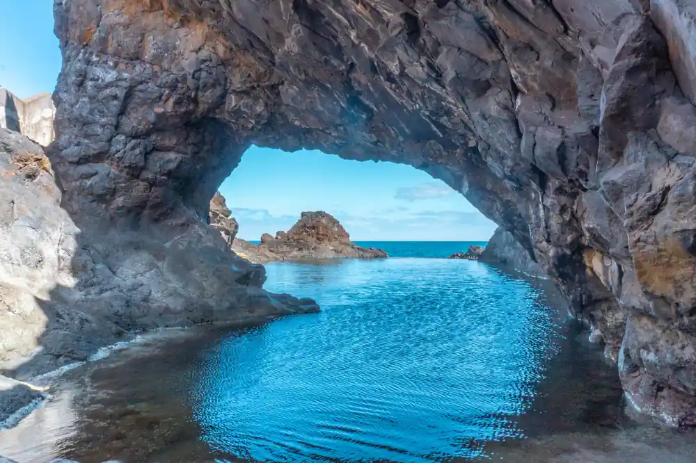 Natural rock arch framing turquoise sea and distant island