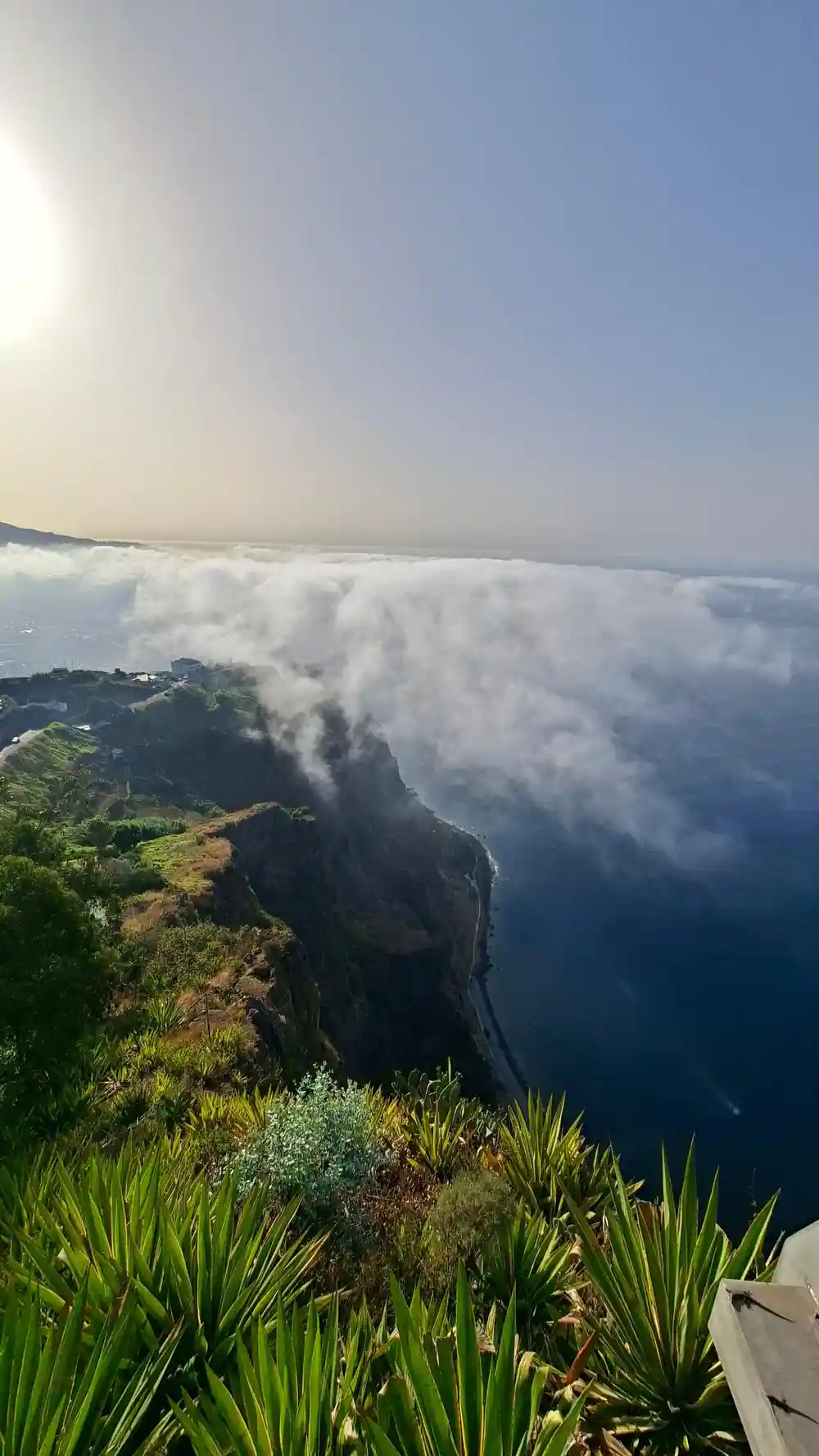 Steep green cliff emerging from clouds over landscape