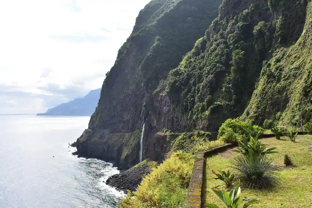 Steep green cliff face with waterfall dropping to ocean