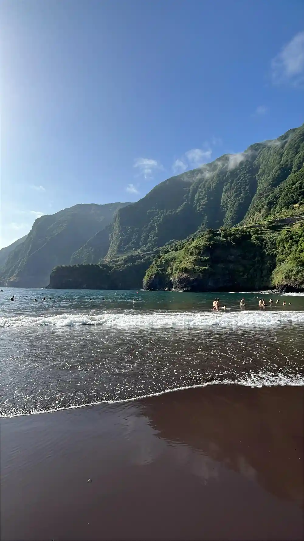 Steep green cliffside meeting black sand beach and turquoise water