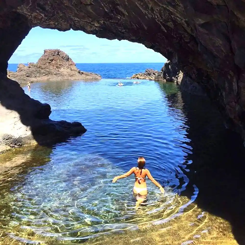 Swimmer in cave opening looking out to turquoise sea and rocks