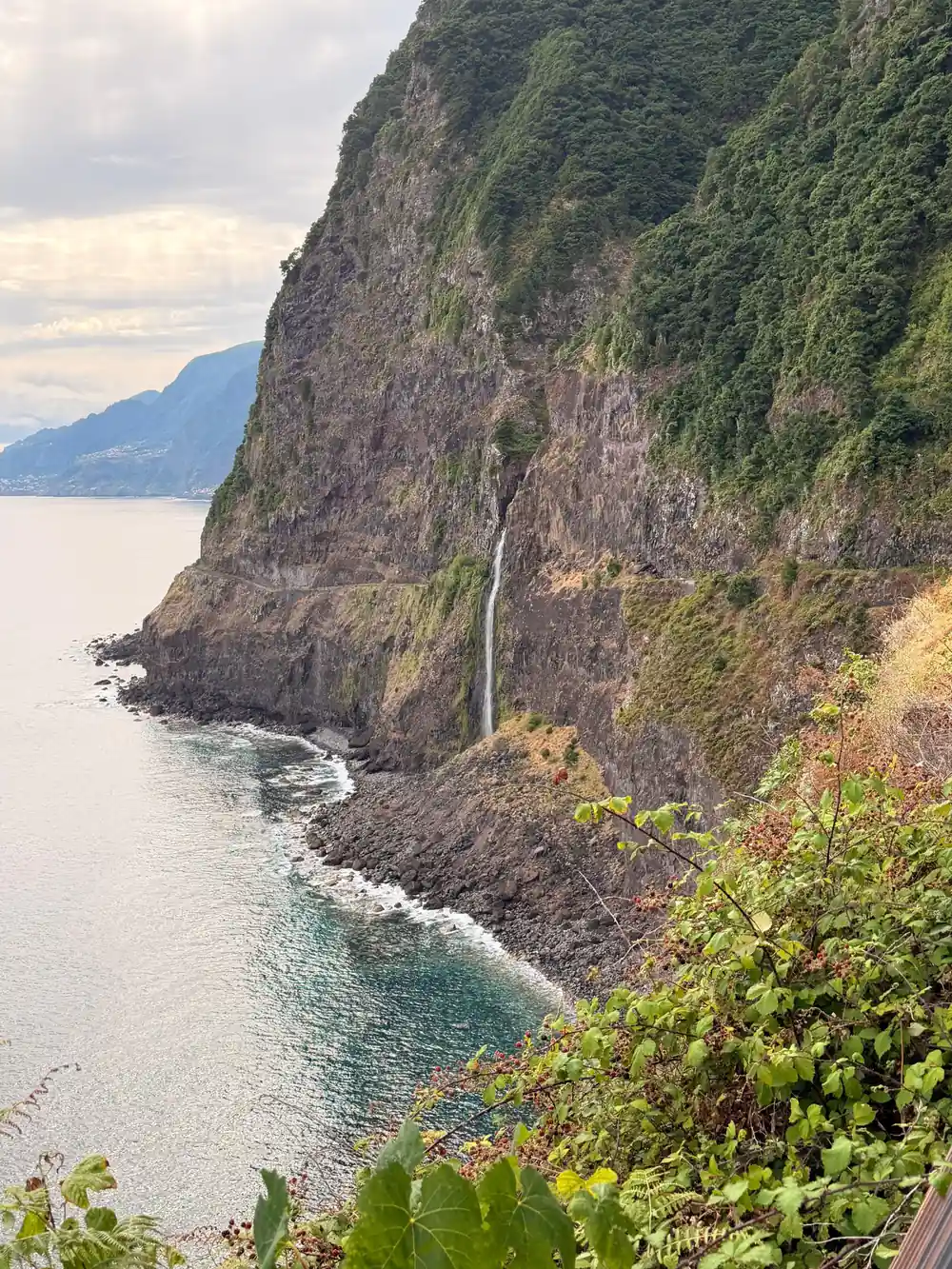 Tall cliff with waterfall dropping to turquoise sea