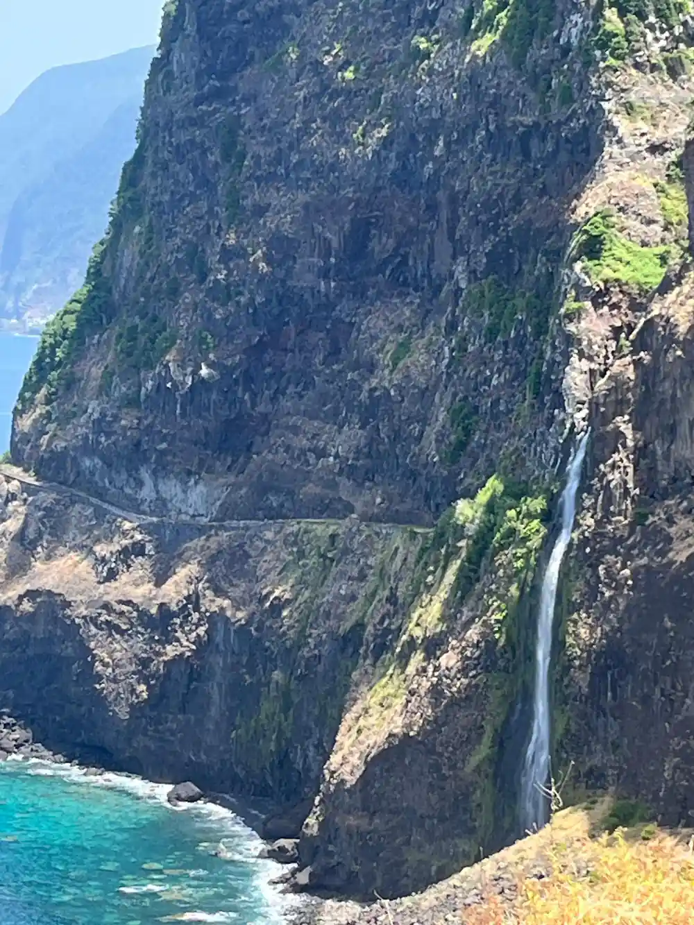 Waterfall cascading down steep green volcanic cliff to ocean