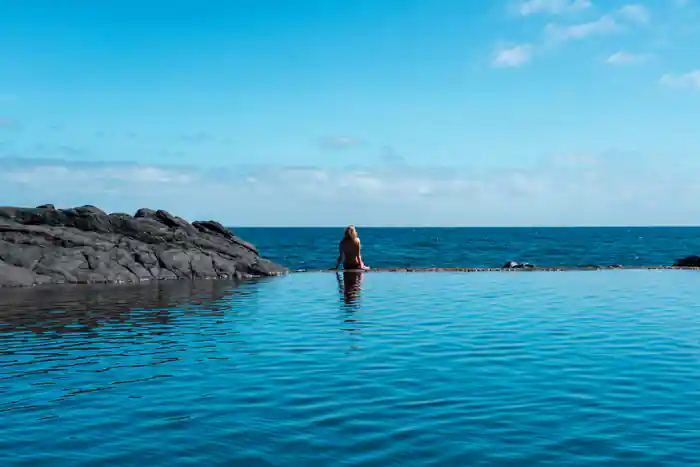 Woman wading in shallow turquoise ocean near rocky outcrop