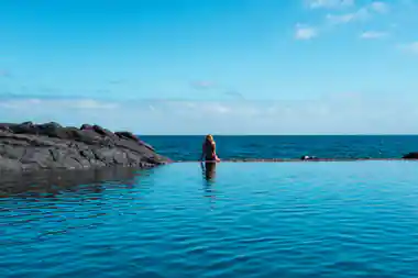 Woman wading in shallow turquoise ocean near rocky outcrop
